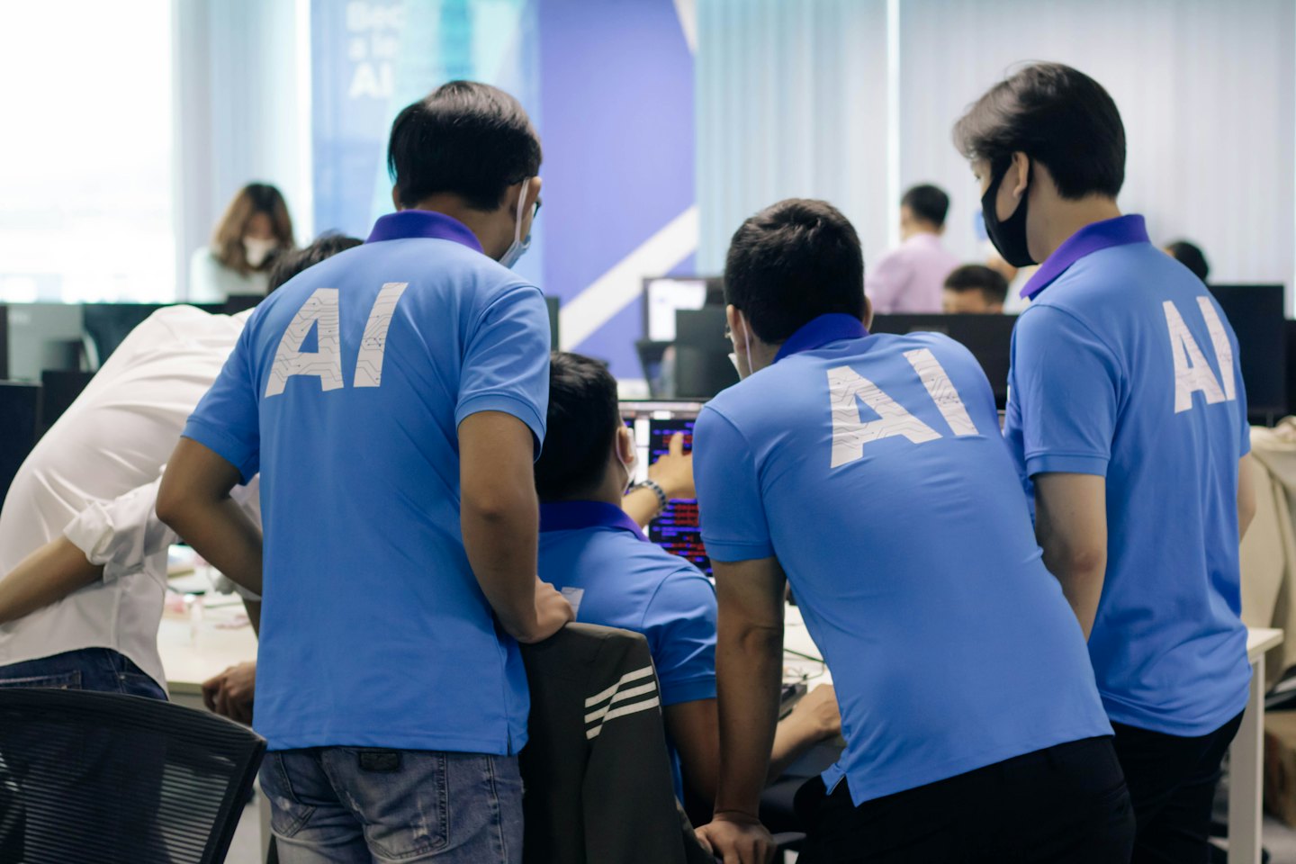 Team members in blue shirts point at a computer screen.